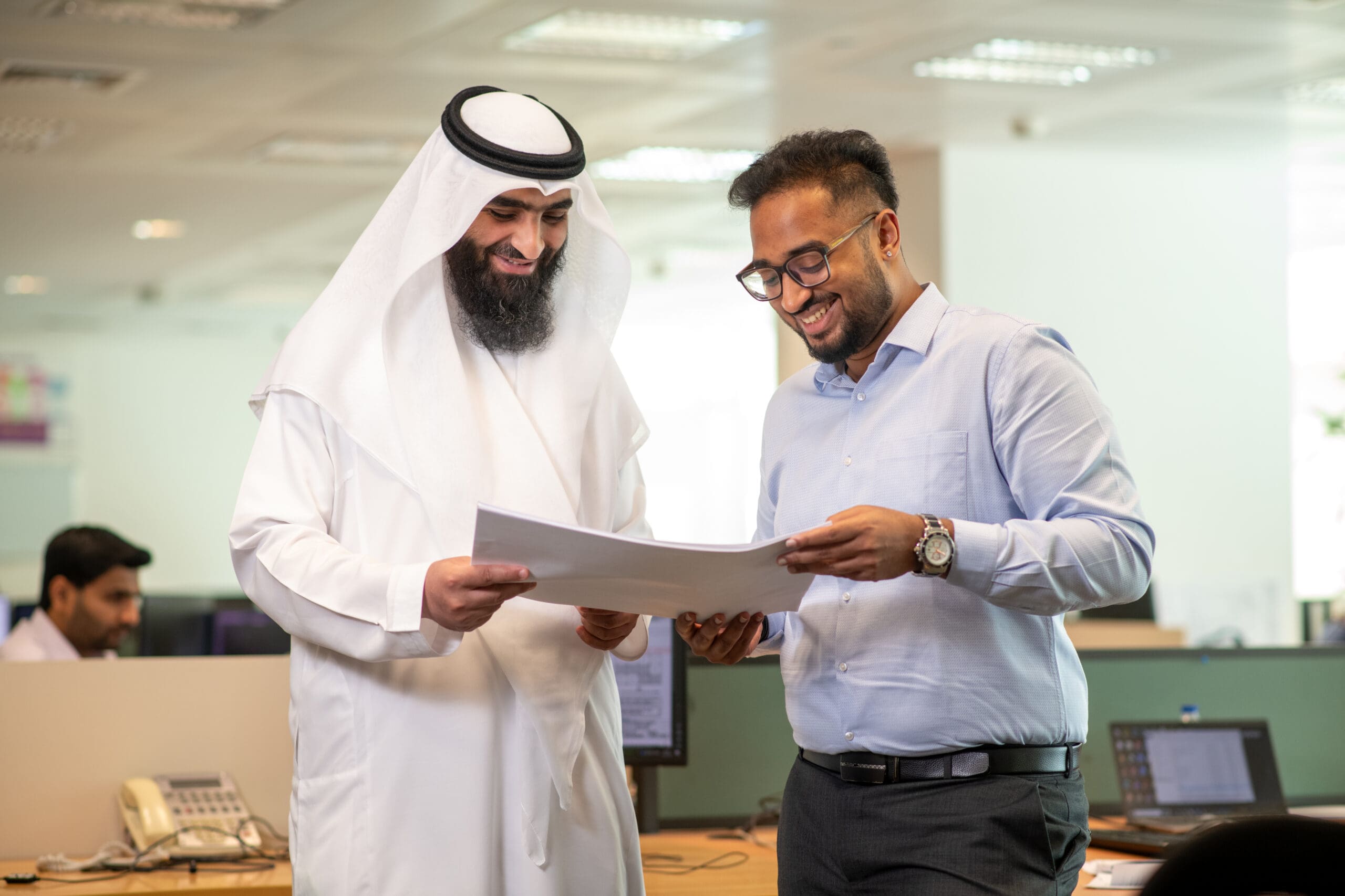 Two men smiling and looking at documents in a office.
