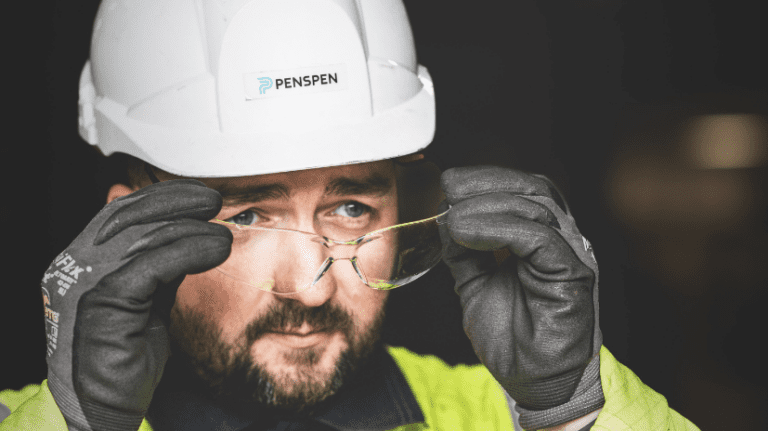 A close up shot of a man in a Penspen hard hat putting on safety glasses.