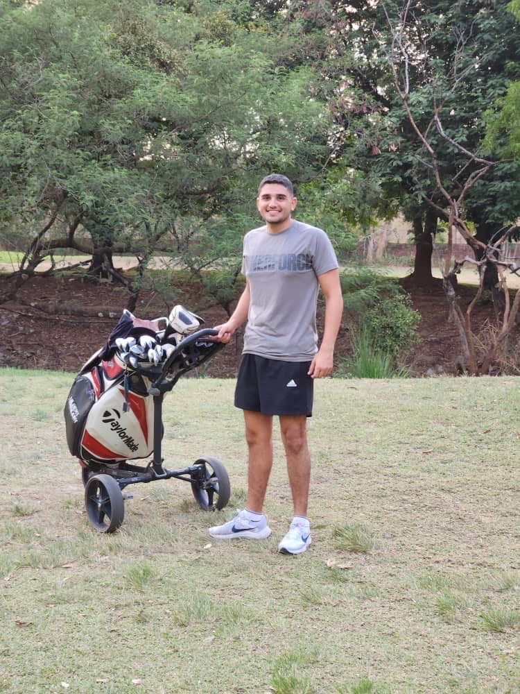 A young man on a golf course next to a bag of golf clubs.