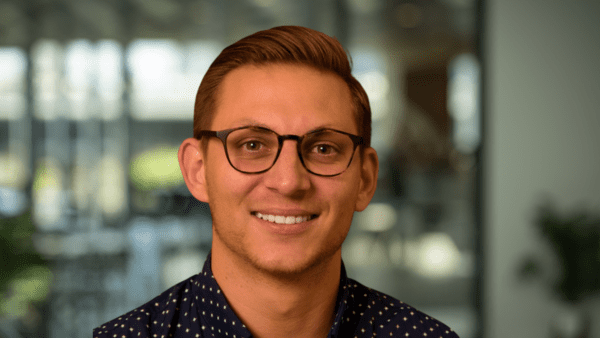 A head and shoulders photo of a male in his 30s wearing glasses