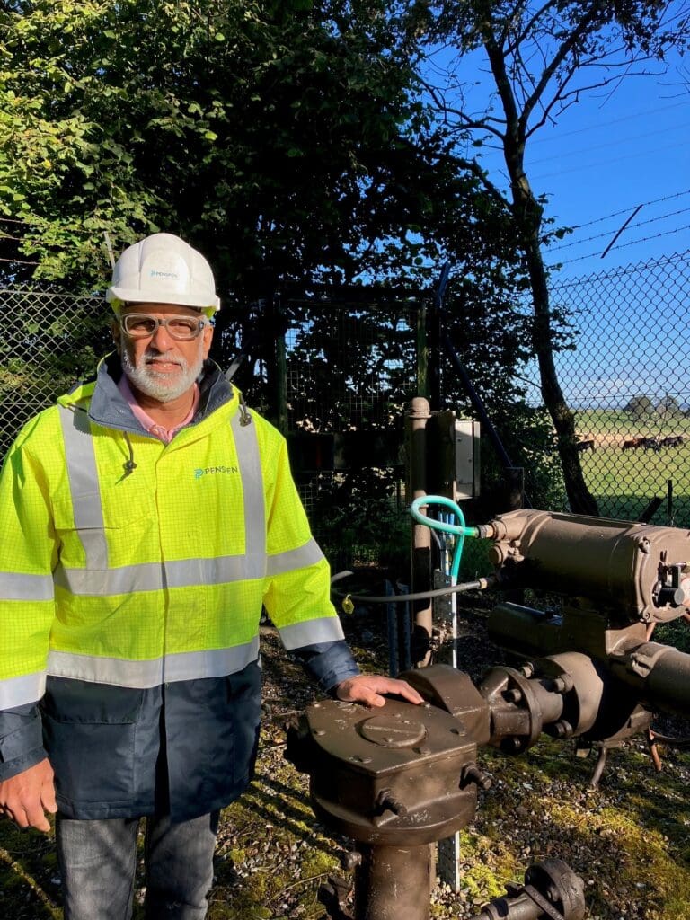 A man in his 60s wearing PPE stands beside gas equipment outside