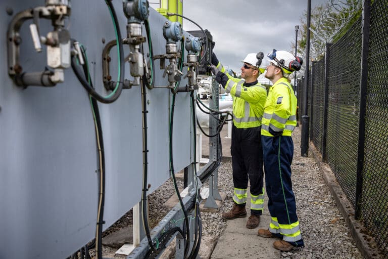 Two male employees in Penspen PPE inspect some equipment at an outdoor site