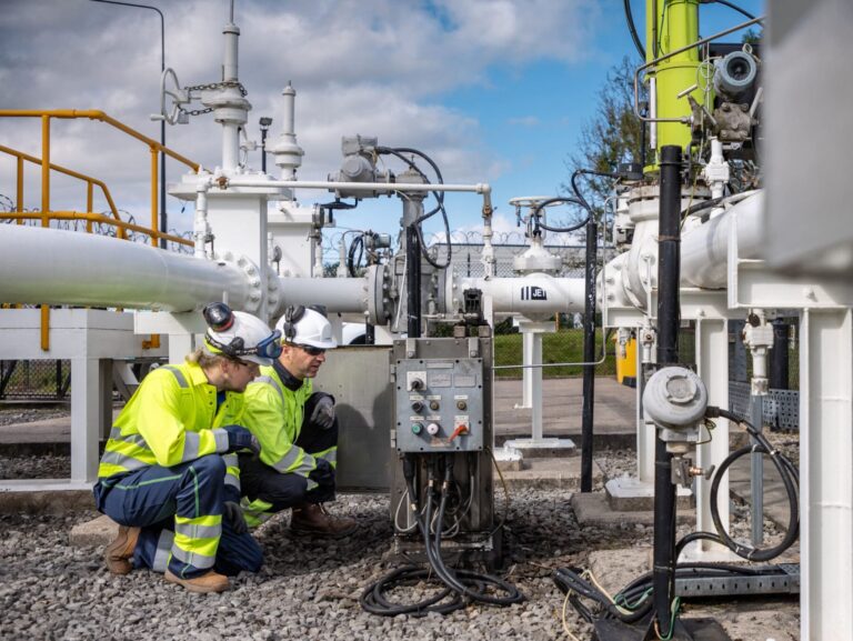 Two men crouch to examine an asset at a fuel pipeline site