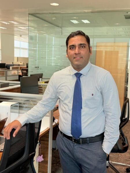 A man stands in an office and smiles at the camera.