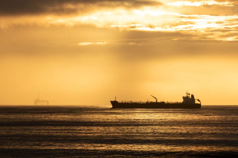 An image of an oil tanker at sunset with an offshore platforn in the background